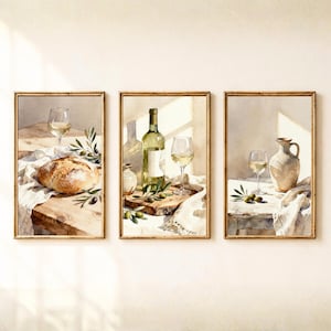 May include: A set of three framed watercolor prints depicting still life scenes. The first shows bread and a wine glass, the second a wine bottle and glass, and the third a ceramic pitcher and wine glass, all accented with green olive branches.