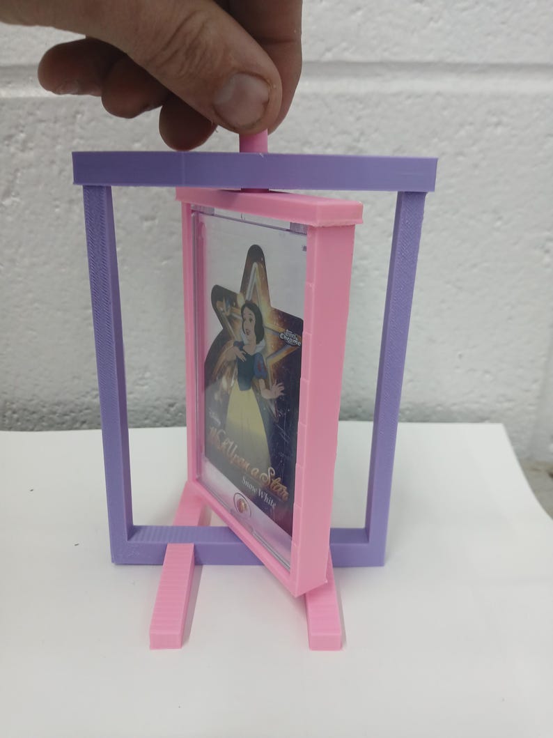 May include: A 3D-printed, pink and purple picture frame with a Snow White image. The frame is supported by two pink legs and a purple rectangular frame. The image is held in a pink frame and is titled "Once Upon a Star".
