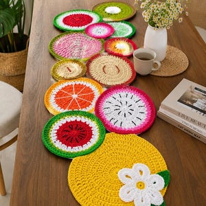 May include: A collection of circular crochet coasters and mats featuring various fruit designs including watermelon, orange, dragon fruit, and lemon patterns. The set includes a large yellow lemon mat with a white flower appliqué and green leaves.