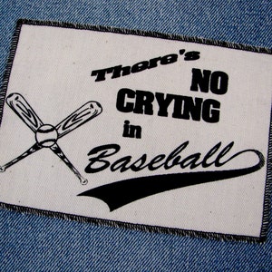 May include: A white patch with black text and a baseball theme. The patch features crossed baseball bats and a baseball, with the words "There's NO CRYING in Baseball."