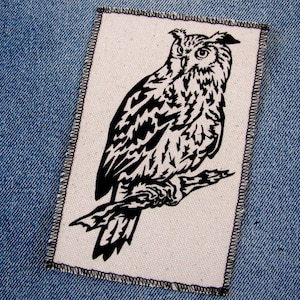 May include: Black and white embroidered patch of an owl perched on a branch. The owl is facing right and has large, round eyes.