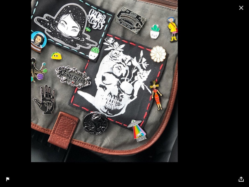 May include: A gray canvas bag with various pins and patches. The patches include a skull with flowers, a black and white illustration of a woman's face, and a patch that says "Put the dogs to sleep".
