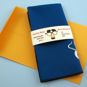 May include: A blue fabric napkin with a white octopus design is wrapped with a white label that reads "Snotty Brat Handmade just for you... Erin Shepard In Dansville, NY".