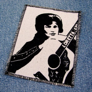 May include: Black and white iron-on patch featuring a singer with a guitar. The guitar has the word "Loretta" written on it.