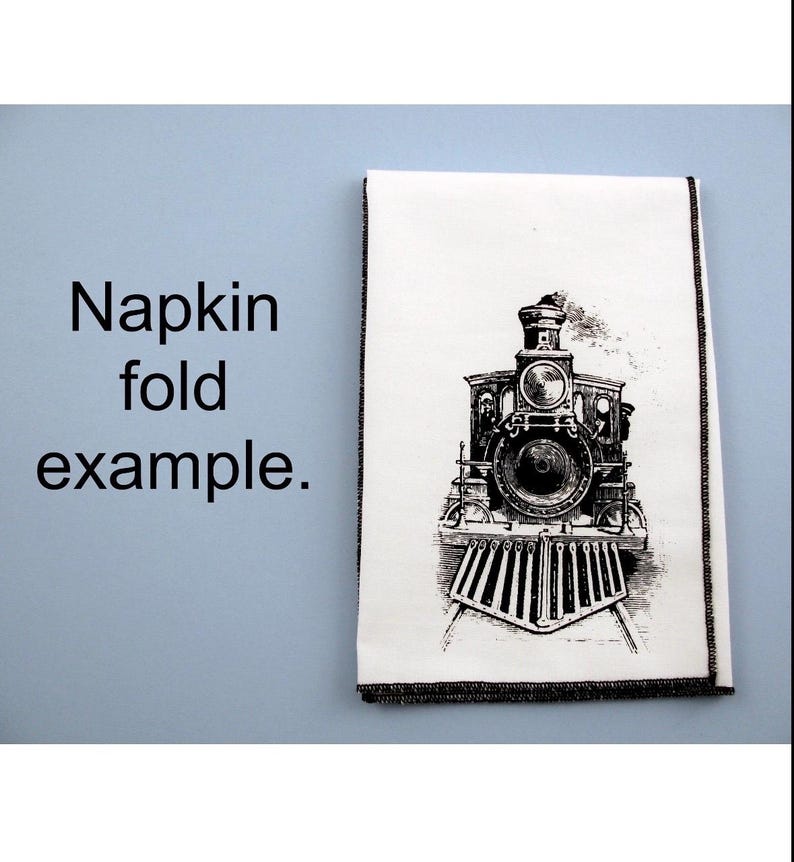 May include: A white napkin with a black and white illustration of a vintage steam locomotive. The napkin is folded in half and has a black border.