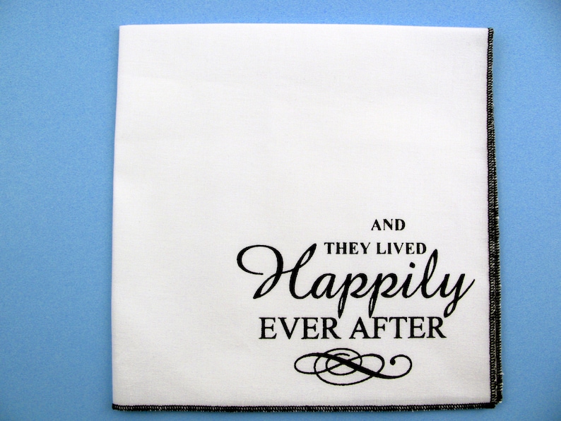 May include: White fabric napkin with black embroidered text that reads "And they lived happily ever after" with a decorative flourish.