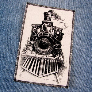 May include: Black and white image of a vintage steam locomotive with a large front wheel and a smokestack. The locomotive is on a set of railway tracks.