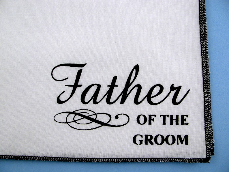 May include: White handkerchief with black embroidered text that reads "Father of the Groom".