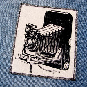 May include: Black and white image of a vintage camera with bellows. The camera is on a tripod and has a lens cap on the lens.