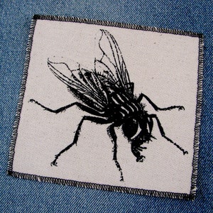 May include: Black and white iron-on patch of a fly on a white background.