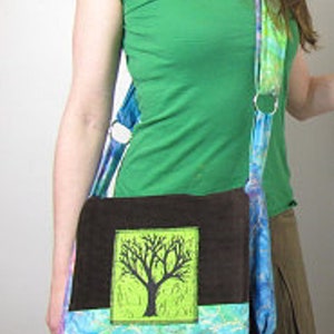 May include: A brown and blue fabric messenger bag with a green and black tree design. The bag has a long strap and a flap closure.