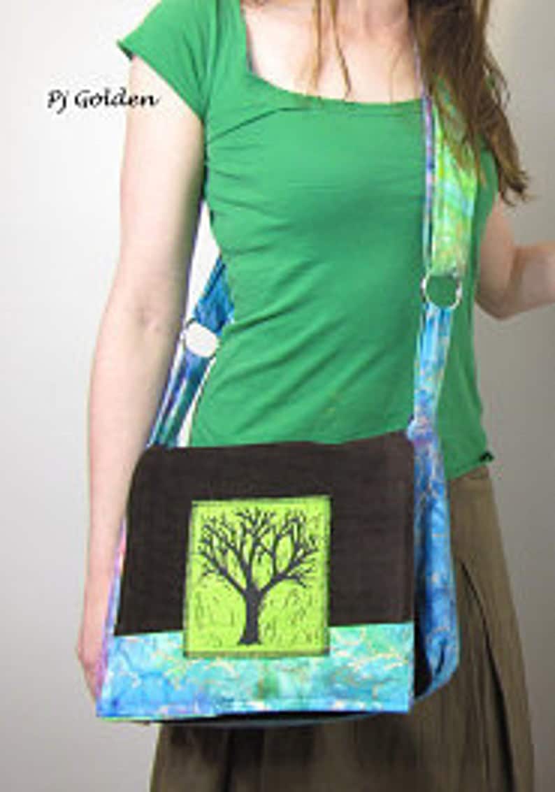 May include: A brown and blue fabric messenger bag with a green and black tree design. The bag has a long strap and a flap closure.
