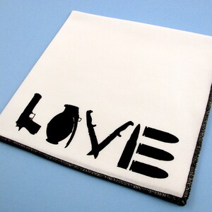 May include: White cloth napkin with black silhouette images of a gun, grenade, knife, and bullets spelling out the word "LOVE".