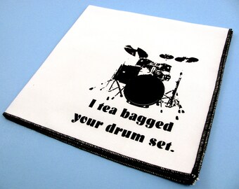 以下が含まれることがあります： 黒い文字で「I tea bagged your drum set.」と書かれた白いお茶のタオルと、黒いシルエットのドラムセット。