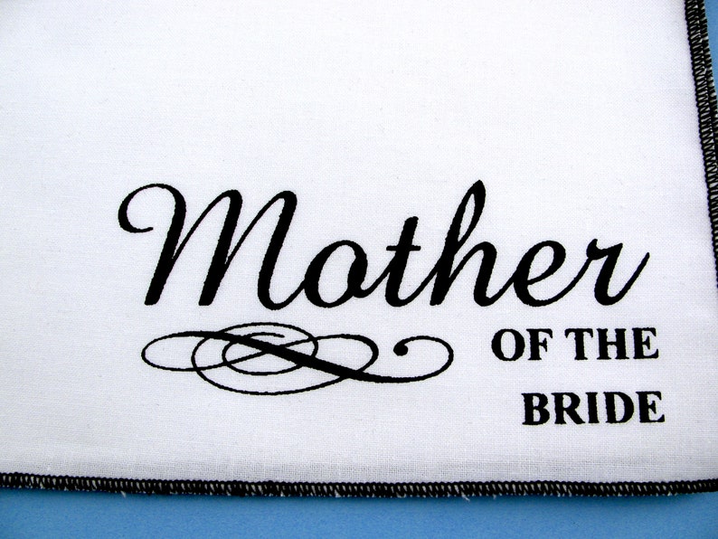 May include: White fabric with black text that reads "Mother of the Bride".