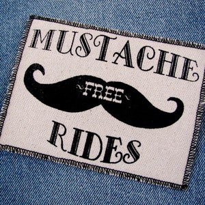 May include: A white patch with black text and a black mustache graphic. The text reads "Mustache Free Rides".