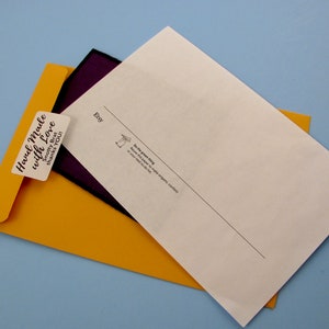 May include: A yellow envelope with a sticker that says "Hand Made with Love" and a smaller sticker that says "Smoochy But Thanks You". The envelope is partially covering a white sheet of paper with the word "Etsy" printed on it.
