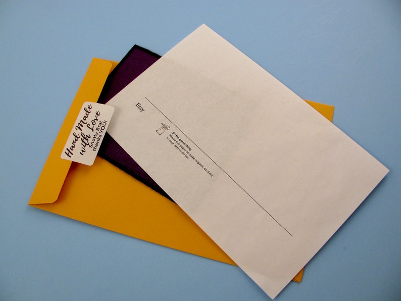 May include: A yellow envelope with a sticker that says "Hand Made with Love" and a smaller sticker that says "Smoochy But Thanks You". The envelope is partially covering a white sheet of paper with the word "Etsy" printed on it.