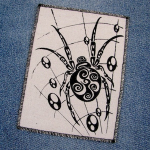 May include: Black and white embroidered patch of a spider with a web design. The spider has a detailed, swirling pattern on its body.