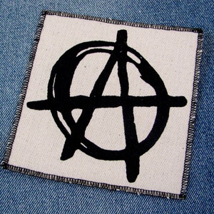 May include: A black and white anarchy symbol patch sewn onto a blue denim fabric.