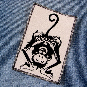 May include: Black and white embroidered patch of a monkey with a curled tail, holding a sign that says "Aloha".