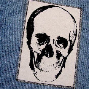Peut inclure: Patch de crâne noir et blanc avec une bordure cousue. Le crâne est imprimé sur un fond de tissu blanc.
