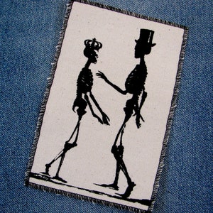 May include: A white fabric patch with two black skeleton figures. One skeleton is wearing a crown and the other is wearing a top hat.