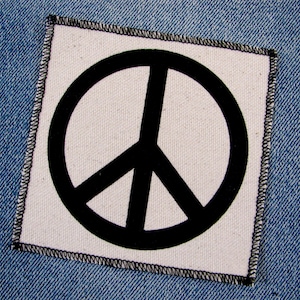 May include: A white fabric patch with a black peace sign sewn onto denim fabric.