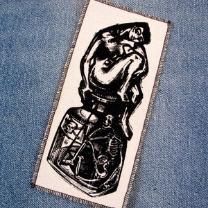 May include: Black and white embroidered patch featuring a stylised image of a person sitting on a bottle with a skull and crossbones design.