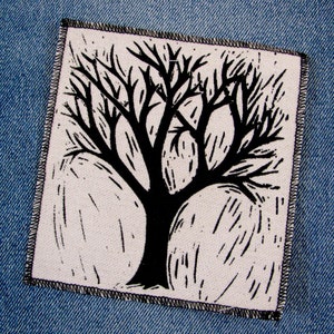 May include: Black and white illustration of a tree with bare branches on a white background. The tree is outlined in black and has a thick trunk. The background is a white fabric with a subtle texture.