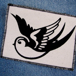 May include: Black and white swallow bird design on a white fabric patch with a black stitched border.