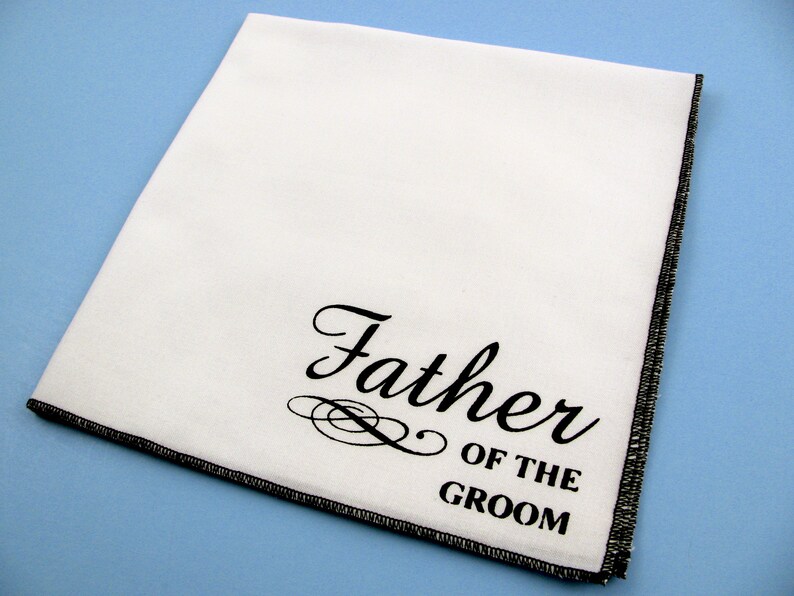 May include: White handkerchief with black embroidered text that reads "Father of the Groom".