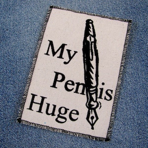 May include: A white fabric patch with black text and a black and white illustration of a pen. The text reads "My Pen is Huge."