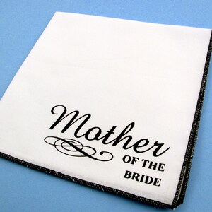 May include: White handkerchief with black embroidered text that reads "Mother of the Bride".