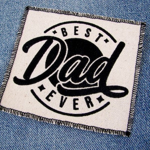May include: A white fabric patch with black stitching around the edges. The patch features a black circle with the text "BEST DAD EVER" in a stylized font.