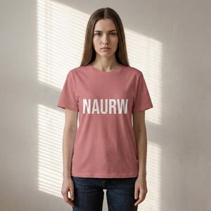 May include: A dusty rose-colored t-shirt with the word "NAURW" printed in bold white capital letters. The shirt has short sleeves and a crew neck. The model is wearing dark blue jeans.