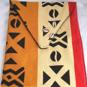 May include: A rectangular fabric clutch with a flap closure. The clutch features a geometric pattern in orange, cream, and red. The flap is secured with two small white seashells. Black shapes and lines decorate the fabric.