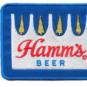 May include: Embroidered patch with a blue border and a white rectangular centre. The patch features the Hamm's Beer logo in red script, with "BEER" in blue block letters. Above the text is a white crown design with yellow accents.