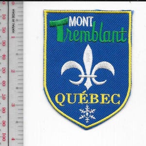 Könnte beinhalten: Blauer, gestickter Aufnäher mit gelbem Rand. Der Aufnäher zeigt die Worte "MONT Tremblant" in Grün, eine weiße Fleur-de-Lis, das Wort "QUÉBEC" in Gelb und eine Schneeflocke. Der Aufnäher ist etwa 7,6 cm hoch.