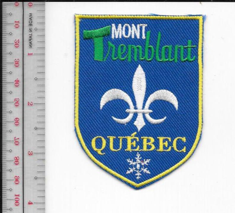Puede incluir: Parche bordado azul con borde amarillo. Presenta las palabras "MONT Tremblant" en verde, una flor de lis blanca, la palabra "QU&Eacute;BEC" en amarillo y un copo de nieve. El parche mide aproximadamente 7,6 cm de alto.