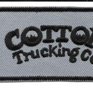 May include: Rectangular patch with the text "COTTON Trucking Co." in black, embroidered on a light gray background. The patch has a black border and is likely for clothing or accessories.