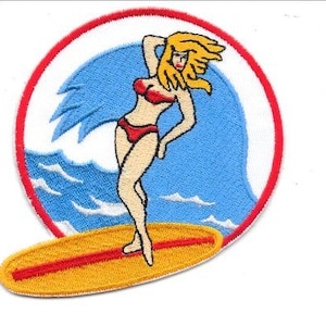 May include: Embroidered patch featuring a woman in a red bikini surfing on a yellow surfboard. The design includes a blue wave, a red circle border, and a white background. The patch is likely for clothing or accessories.
