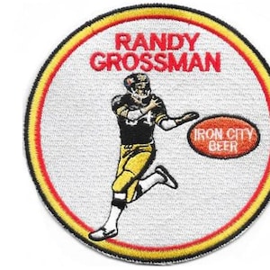 May include: A circular embroidered patch featuring a football player in a black and yellow uniform. The text RANDY GROSSMAN appears above the player, and IRON CITY BEER is in an oval. A ruler shows the patch is approximately 9 cm wide.