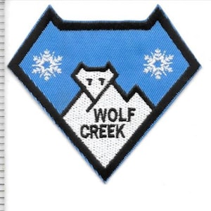Peut inclure: Écusson brodé bleu et blanc en forme de losange avec l'inscription "WOLF CREEK". Il représente un loup au-dessus d'une chaîne de montagnes et deux flocons de neige.