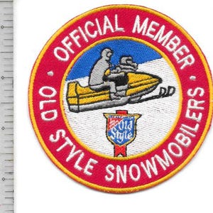 Op de afbeelding: Een ronde patch met een rode rand en witte tekst met de tekst "OFFICIAL MEMBER OLD STYLE SNOWMOBILERS". Het midden toont een gele sneeuwscooter met een bestuurder, tegen een blauwe lucht. Onderaan staat een klein embleem.