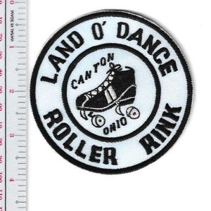 Puede incluir: Un parche circular con un diseño en blanco y negro. El texto "LAND O' DANCE ROLLER RINK" rodea un gráfico de patines negros. También se incluyen las palabras "CANTON OHIO".