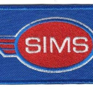 Puede incluir: Un parche rectangular azul con la palabra "SIMS" en letras blancas dentro de un óvalo rojo. El óvalo está bordeado por un borde blanco y flanqueado por diseños blancos en forma de alas. El parche tiene un borde azul.