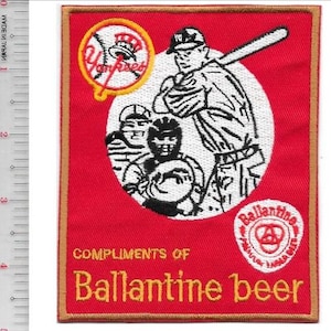 Puede incluir: Un parche rectangular rojo bordado con un jugador de béisbol y un receptor en un círculo blanco, un logotipo de los Yankees y el texto "COMPLIMENTS OF Ballantine beer". Una regla muestra que el parche mide unos 11,5 cm de alto y 9 cm de ancho.