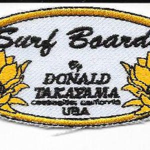 May include: Oval embroidered patch with the words "Surf Boards" in black script. Below the text is "DONALD TAKAYAMA" and "COSTA MESA, CALIFORNIA USA". The patch has a yellow border and two yellow flower designs.