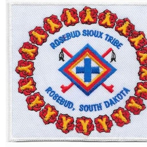 May include: A square embroidered patch featuring the Rosebud Sioux Tribe emblem with a central blue cross, red and yellow diamond, and crossed red staffs. A circular border of red and yellow flowers surrounds the text. A ruler shows a 3-inch width.